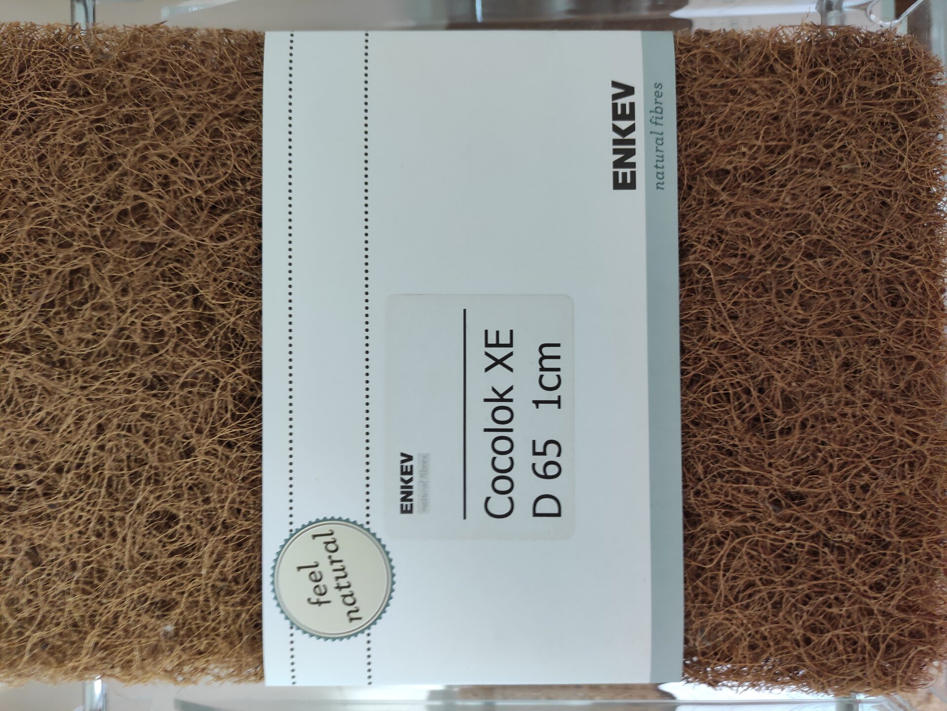 Zdjęcie przedstawia cienkie liczne włókna kokosowe uformowane w prostokąt i opakowane w papierową etykietę z napisem.