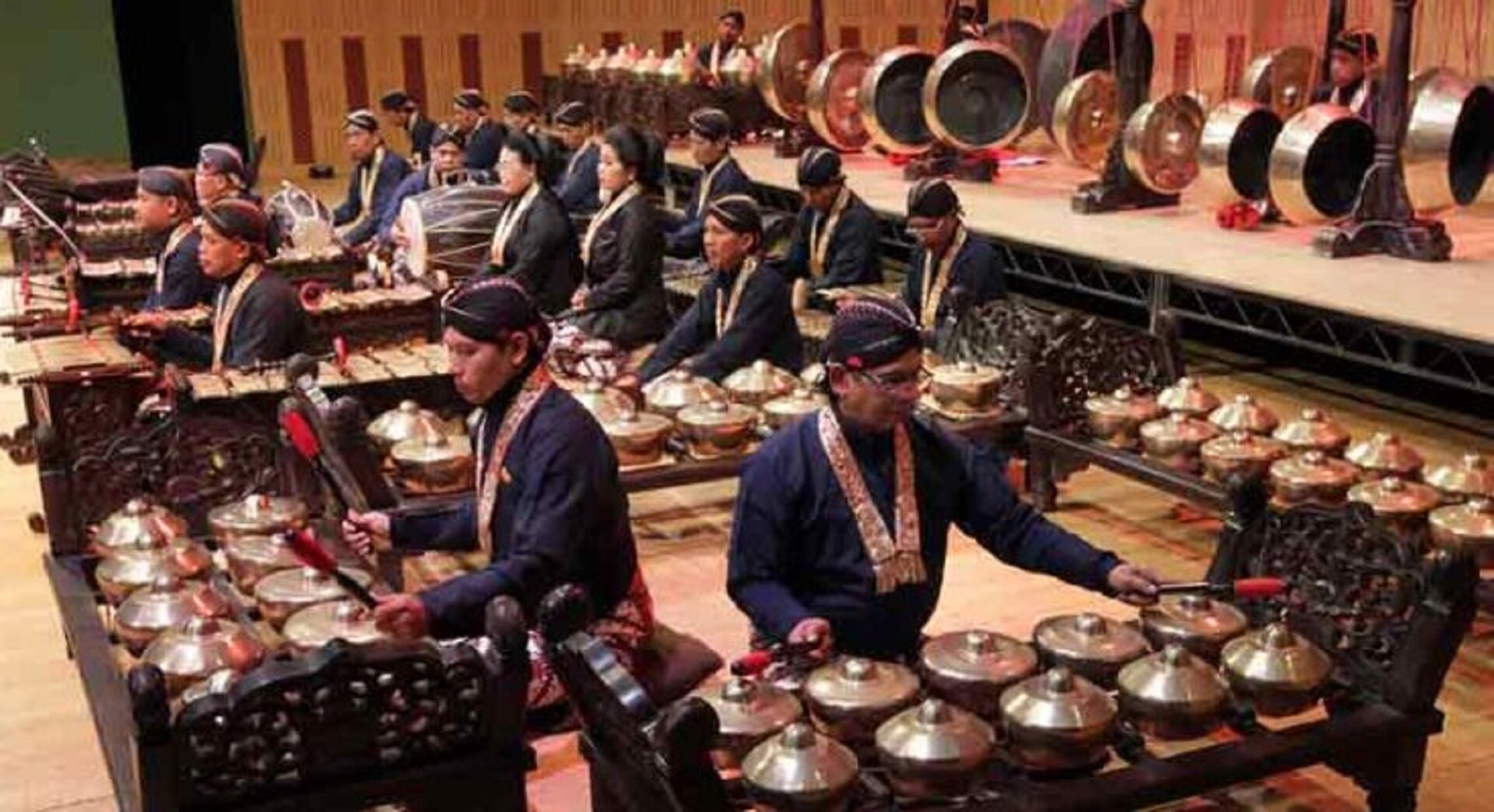 Zdjęcie przedstawiające indonezyjskich muzyków, grających na instrumentach przypominających ławki na których ułożone są koło siebie gongi. Gong jest to wisząca lub ustawiona na specjalnym stojaku tarcza z brązu lub mosiądzu, o wypukłej, czasem falistej powierzchni i lekko zagiętych brzegach.