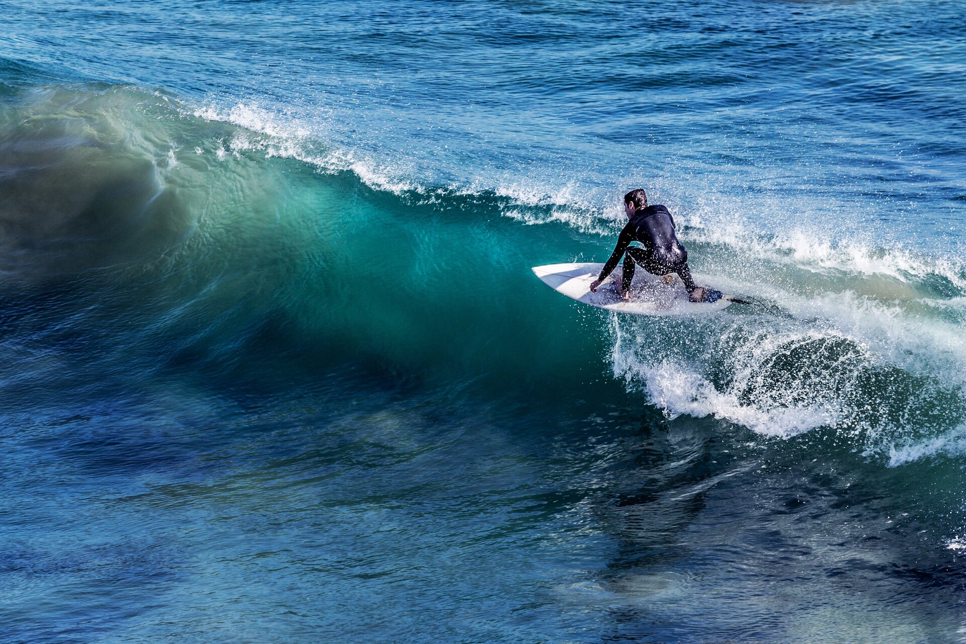 Rys. a. Na zdjęciu widoczny jest fragment morza, przez które przemieszcza się fala o dużej wysokości. Na grzbiecie fali płynie osoba na desce surfingowej.