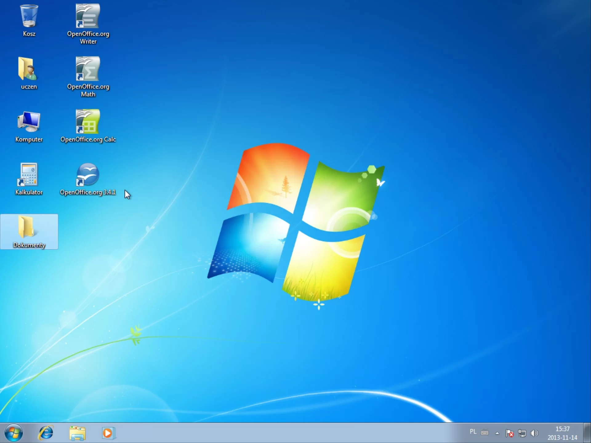 Na zdjęciu przedstawiono zrzut pulpitu dla systemu Windows 7. Na zdjęciu widać niebieską tapetę z centrycznie narysowanym logiem Windows. Na tapecie, w lewym górnym rogu znajdują się w dwóch rzędach ikony podpisane jako: kosz, uczeń, komputer, kalkulator, dokumenty, Open Office org Writer, Open Office org Math, Open Office org Calc Open Office org trzy kropka cztery kropka jeden.Poniżej tapety znajduje się pasek narzędzi. Po lewej stronie paska znajduje się ikony: okrąg z logiem Windows w środku, literka: e z orbitą, żółty folder na dokumenty, biały trójkąt w żółtym kole które jest wpisane w kwadrat. Z prawej strony znajdują się ikony: napis PL, klawiatura, biały trójkąt po rozwinięciu którego pojawiają się dodatkowe opcje, flaga na maszcie poniżej której jest biały krzyżyk wpisany w czerwone koło, ekran z kablem LAN, głośnik, godzina i data przykładowo piętnasta trzydzieści siedem, dwutysięczny trzynasty listopad czternaście.