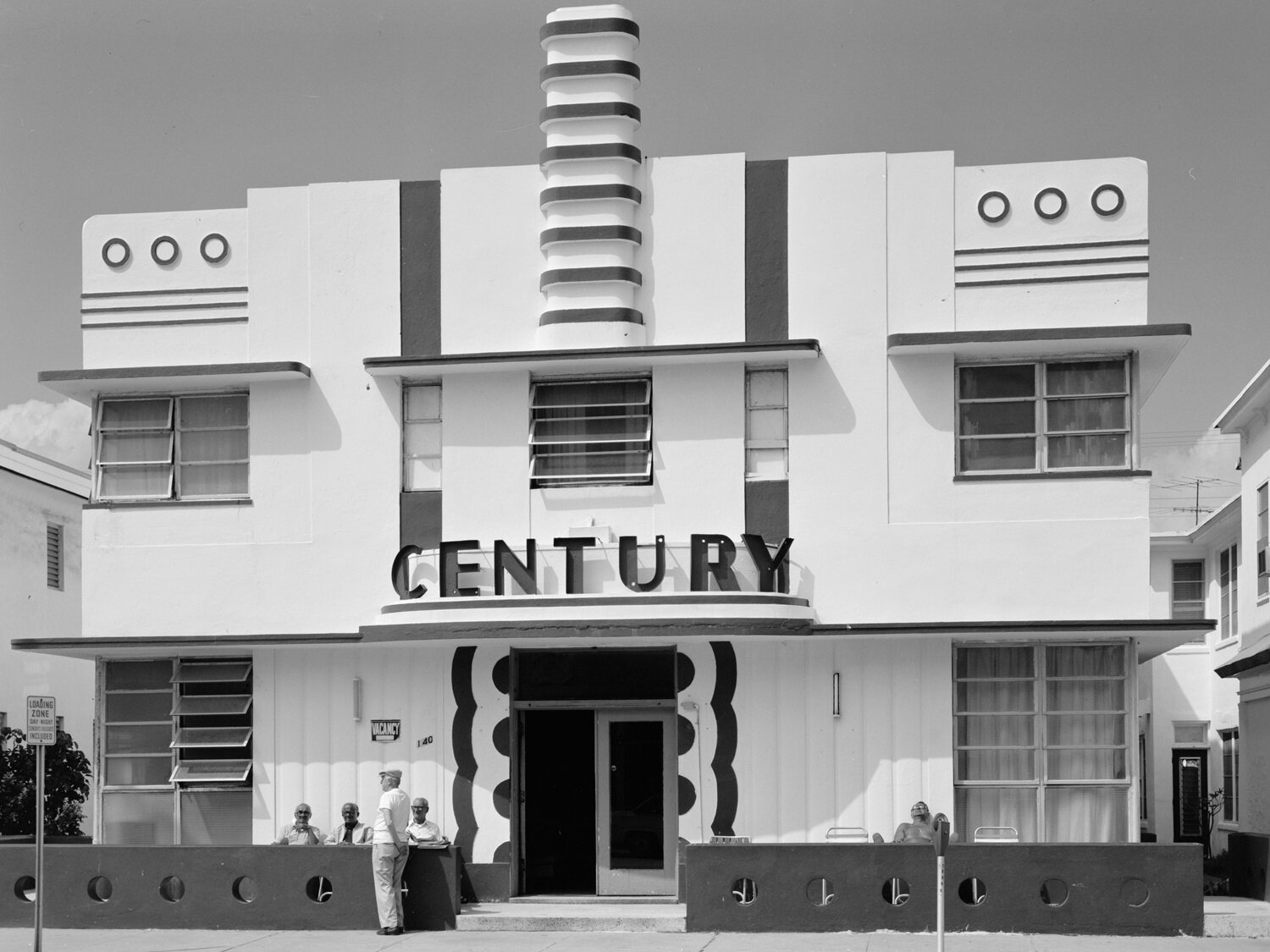  Zdjęcie przedstawia piętrowy budynek o prostokątnej fasadzie. Widoczne jest proste wejście, nad którym na niewielkim, półokrągłym zadaszeniu widoczny jest napis:  CENTURY.  Na parterze i piętrze widoczne są okna złożone z wąskich szyb. Pośrodku budynku u góry wystaje żeberkowany pionowy element.
