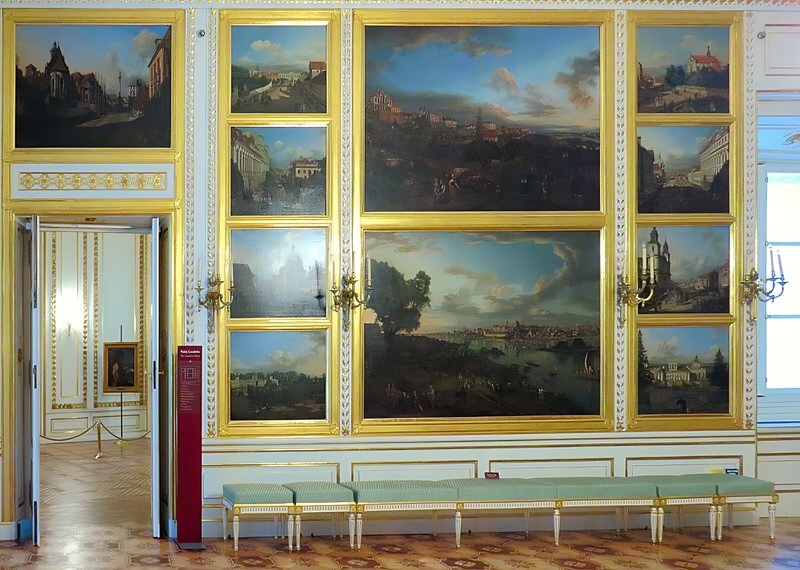 Kliknij, aby powiększyć Zdjęcie przedstawia ścianę Sali Canaletta z wedutami Bernarda Bellotto Canaletta. Nad drzwiami znajdującymi się po lewej stronie jest widoczny obraz „Widok kościoła Bernardynek i kolumny Zygmunta III od strony zjazdu do Wisły”. Na prawo od niego wiszą: od góry w dół- „Pałac Błękitny”, „Ulica Miodowa”, „Kościół Sakramentek” i „Pałac w Wilanowie od strony południowej”. Na prawo od nich jest „Widok Warszawy z Pałacem Ordynackim”, a pod nim „Widok Warszawy od strony Pragi”. Na prawo od tych obrazów jest: od góry w dół- „Kościół Reformatów”, „Ulica Długa”, „Kościół św. Krzyża” i „Pałac w Wilanowie od strony ogrodu”. Obrazy umieszczone są w złotych ramach, między rzędami obrazów umieszczone są kandelabry. Białe ściany sali ozdabiają dodatkowo złocone ornamenty.