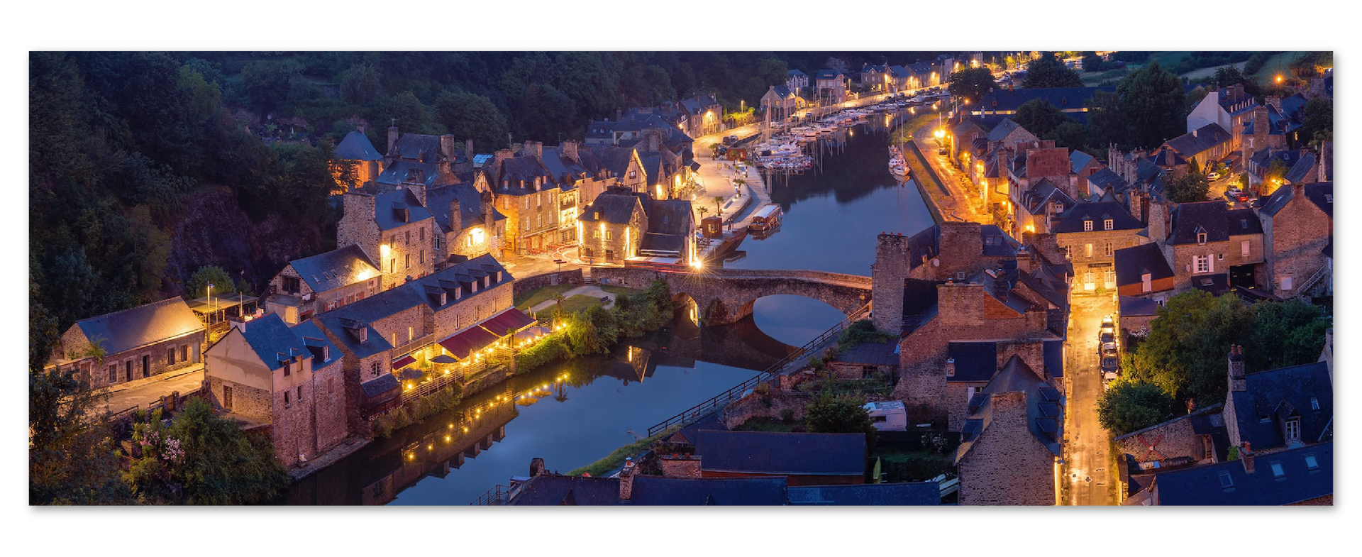 Zdjęcie przedstawia widok z lotu ptaka na miasto nocą. Miasto usytuowane jest po dwóch stronach rzeki. Budynki są zabytkowe, oświetlone. 