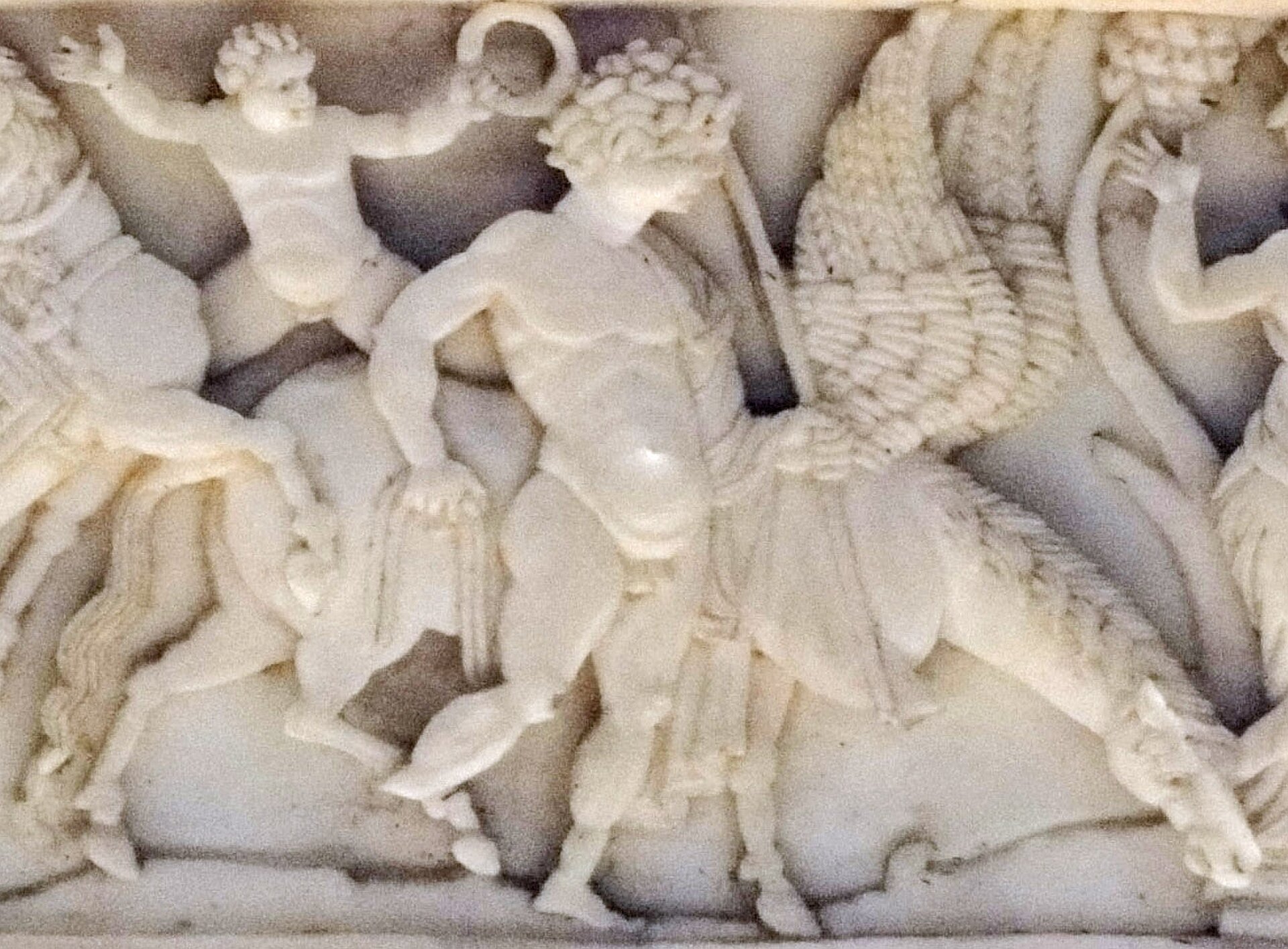 Ilustracja przedstawia detal z sarkofagu Veroli, na którym widoczny jest Bellerofont z Pegazem. Mężczyzna ma krótkie kręcone włosy i stoi obok Pegaza, który pije wodę. Fragment rzeźby jest wykonany z białego materiału.