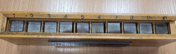 Na zdjęciu widoczna jest skala wzorców Jernkontoret. W drewnianym pudełku widocznych jest dziesięć otworów. W otworach umieszczone są prostopadłościenne wzorce stali. Na górnej powierzchni wzorca próbki widoczne są różnice w wielkości ziarna. Próbka oznaczona cyfra jeden ma najgrubsze ziarno a próbka oznaczona cyfrą dwa najmniejsze.