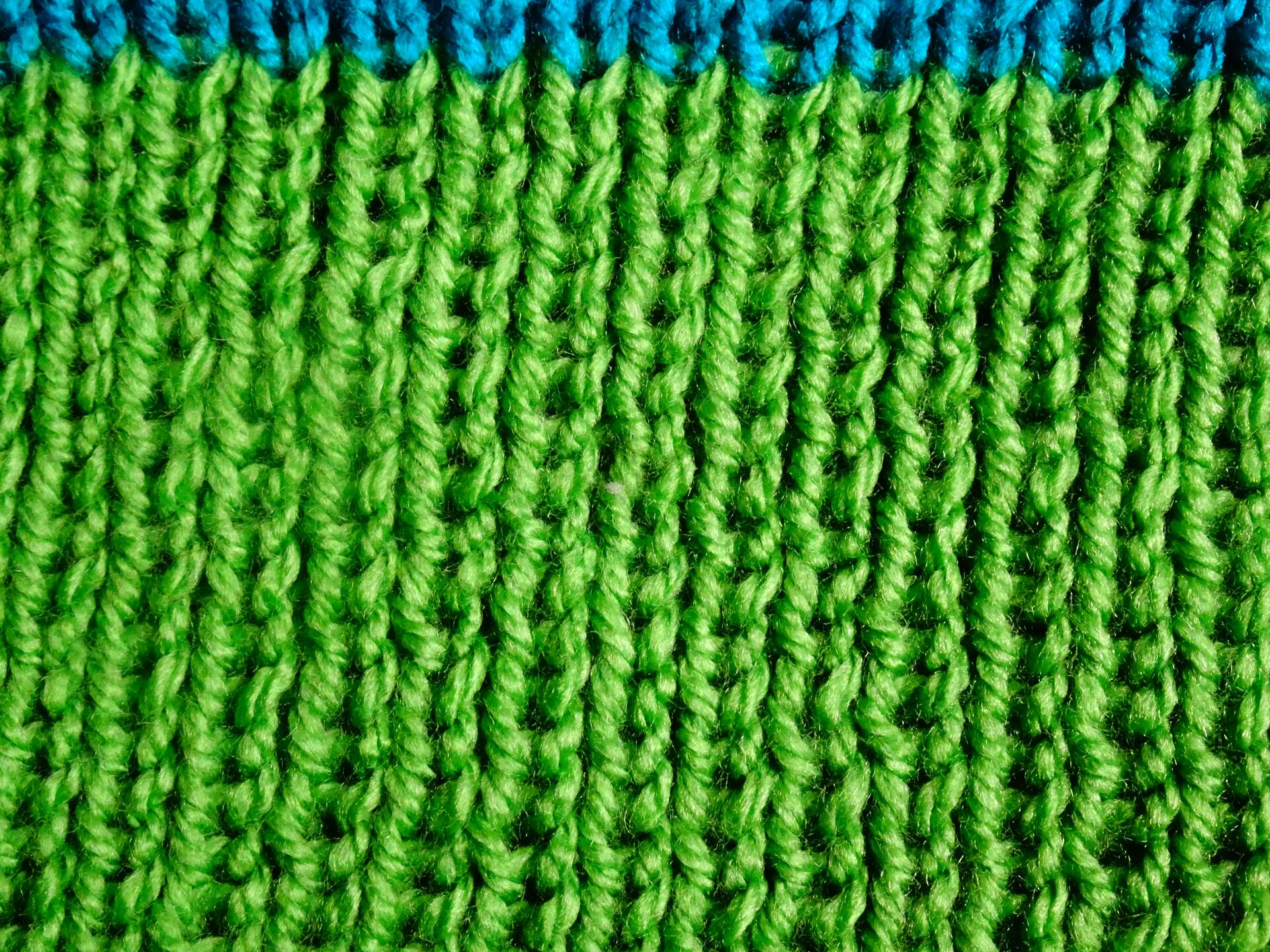 Zdjęcie przedstawia zbliżenie na zieloną dzianinę wykonaną splotem dwuprawym.