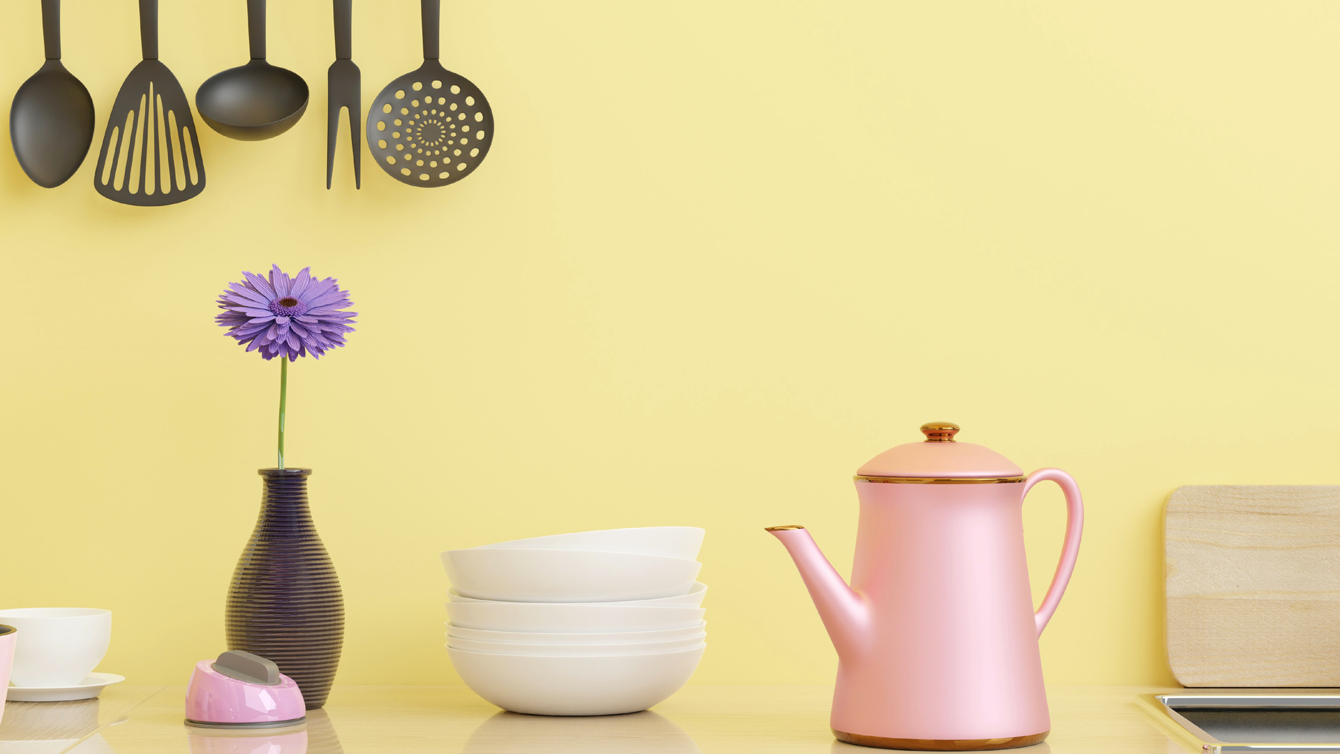 Zdjęcie przedstawia przedmioty codziennego użytku. Od lewej znajduje się filiżanka, następnie wazon z kwiatkiem w środku, dalej widoczny jest stos miseczek porcelanowych. Kolejny stoi porcelanowy dzbanek z pokrywką i drewniana deska. Nad naczyniami, na ścianie wiszą przyrządy kuchenne np,: łyżka wazowa, łyżka cedzakowa.