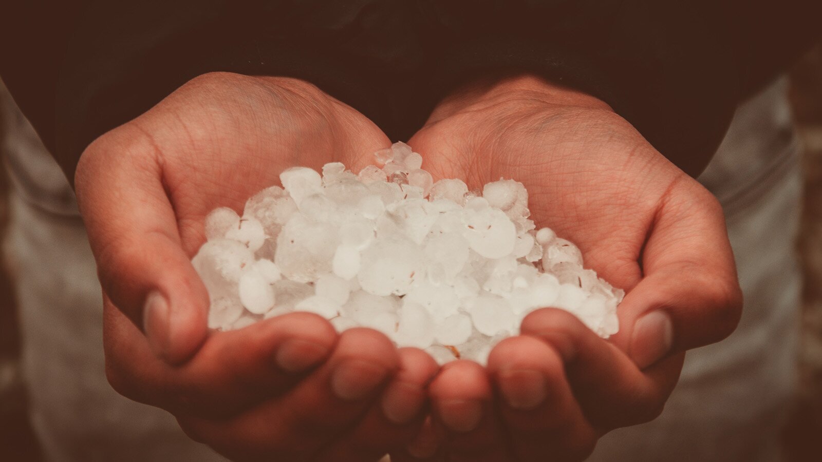 Zdjęcie przedstawia dwie złożone dłonie, które utworzyły zagłębienie. W środku zagłębienia widoczne są kulki gradu o różnej wielkości. 