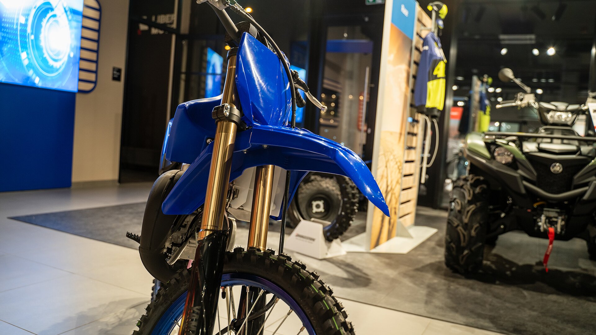 Zdjęcie przedstawia motocykl - widok z przodu - o lekkiej ramie. Motocykl jest wąski, ma bardzo wąskie siedzenie, wysoko nad przednim kołem uniesiony błotnik. Bieżnik na oponie jest głęboki. 