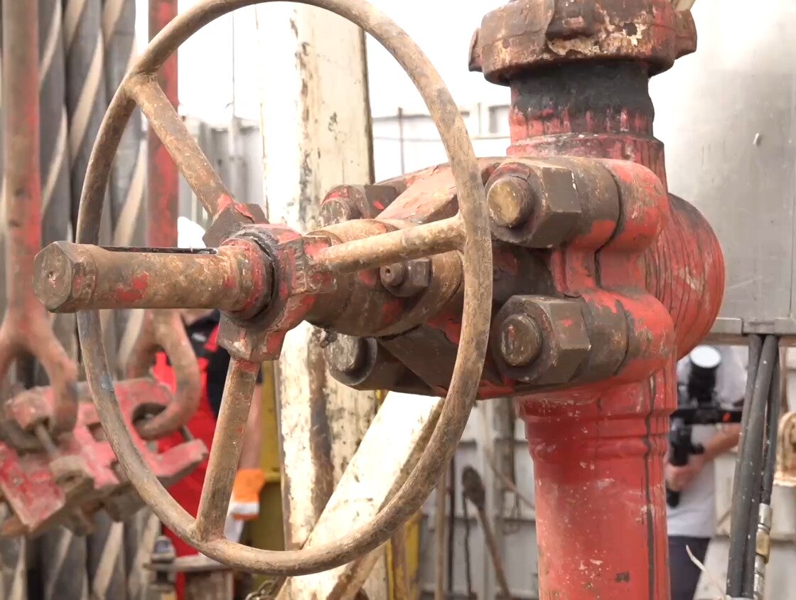 Zasuwa na stojaku płuczkowym zasuwa na stojaku płuczkowym. W centralnej części zdjęcia widoczna jest pionowa rura. Na rurze zamontowana jest zasuwa. Zasuwa jest w  formie dużego okrągłego pokrętła. Pokrętło przymocowane jest do rury pięcioma śrubami.Poniżej zdjęcia w prawym dolnym rogu widoczny jest przycisk odtwarzania. Tekst nagrania jest zgodny z tytułem zdjęcia.