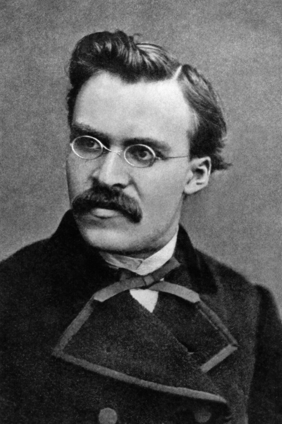 Zdjęcie przedstawia portret młodego mężczyzny. Jego twarz jest pociągła. Mężczyzna ma ciemne, proste, zaczesane ku górze włosy. Ma założone druciane, owalne okulary. Na jego twarzy widnieją gęste, długie wąsy. Ubrany jest w surdut, koszulę. Pod szyją ma zawiązaną wąską wstążkę.