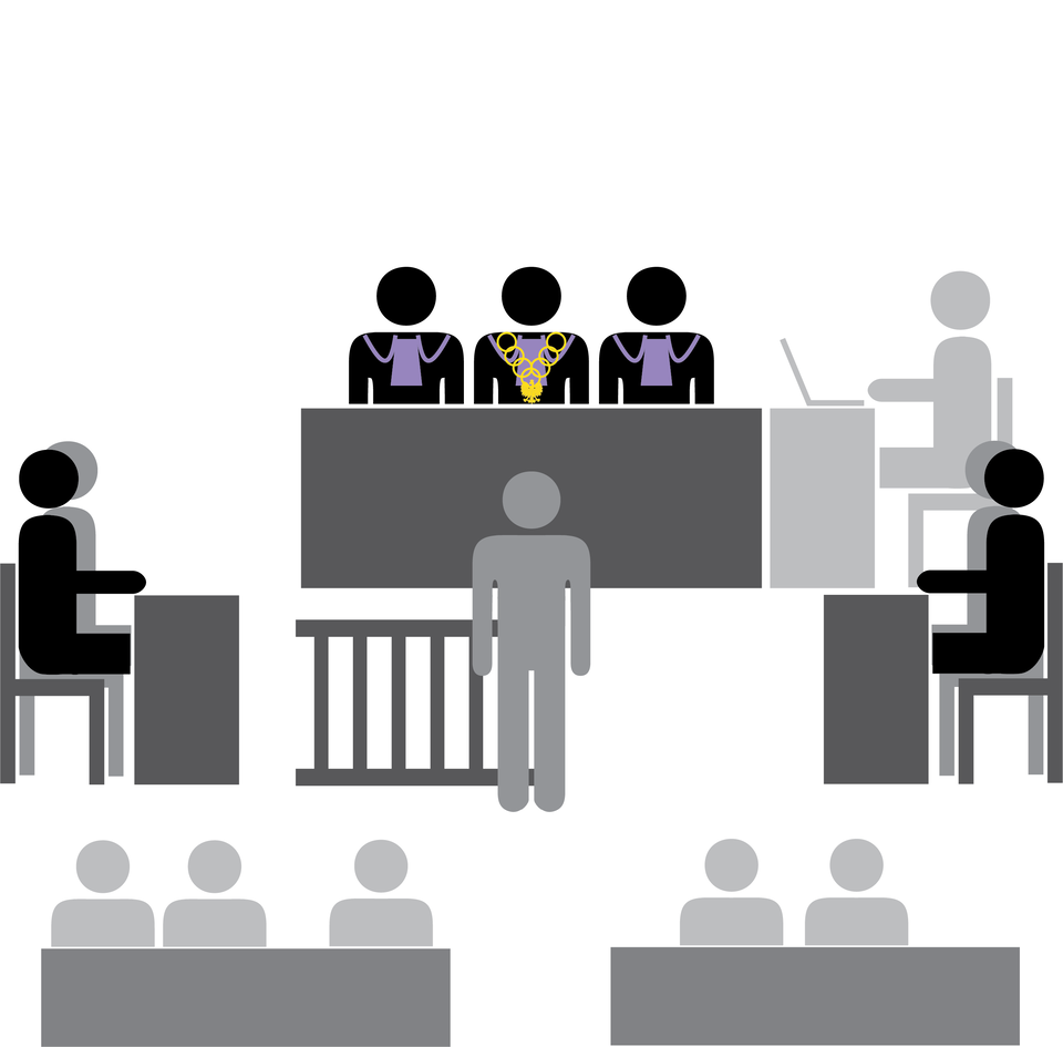 Grafika przedstawia salę sądową. Zasiada w niej trzyosobowy sąd, osoba notująca na komputerze przebieg toczącej się sprawy i dwie strony procesowe. Przed sądem zeznaje jedna osoba. Widać także publiczność zasiadającą w ławach.