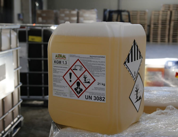 Zdjęcie przedstawia plastikowy kanister z cieczą w środku. Na kanistrze znajdują się następujące trzy oznaczenia. Pierwsze biały romb podzielony na cztery równe romby, każdy z czerwoną obwódką i czarnymi rysunkami wewnątrz. Mniejsze romby są następujące. W pierwszy znajduje się rysunek dwóch probówek, z których wylewa się ciecz na powierzchnię płaską i na ludzką dłoń. Powierzchnia i dłoń parują. W drugim małym rombie znajduje się martwe drzewo bez liści i ryba leżąca na grzbiecie, mająca otwarty pyszczek. W trzecim małym rombie znajduje się popiersie człowieka. Na wysokości przełyku znajduje się biała kula, od której odchodzą w różne strony błyskawice. W czwartym małym rombie znajduje się wykrzyknik. Oznaczenie drugie jest białym rombem z podwójną czarną obwódką. Zewnętrzna narysowana jest linią przerywaną, wewnętrzna ciągłą. Górna połowa rombu jest w białe i w czarne pionowe pasy o równej szerokości. Dolna jest biała. W dolnym rogu znajduje się cyfra dziewięć. Trzecie oznaczenie to biały romb z czarną obwódką. W nim martwe drzewo bez liści i ryba leżąca na grzbiecie, mająca otwarty pyszczek.