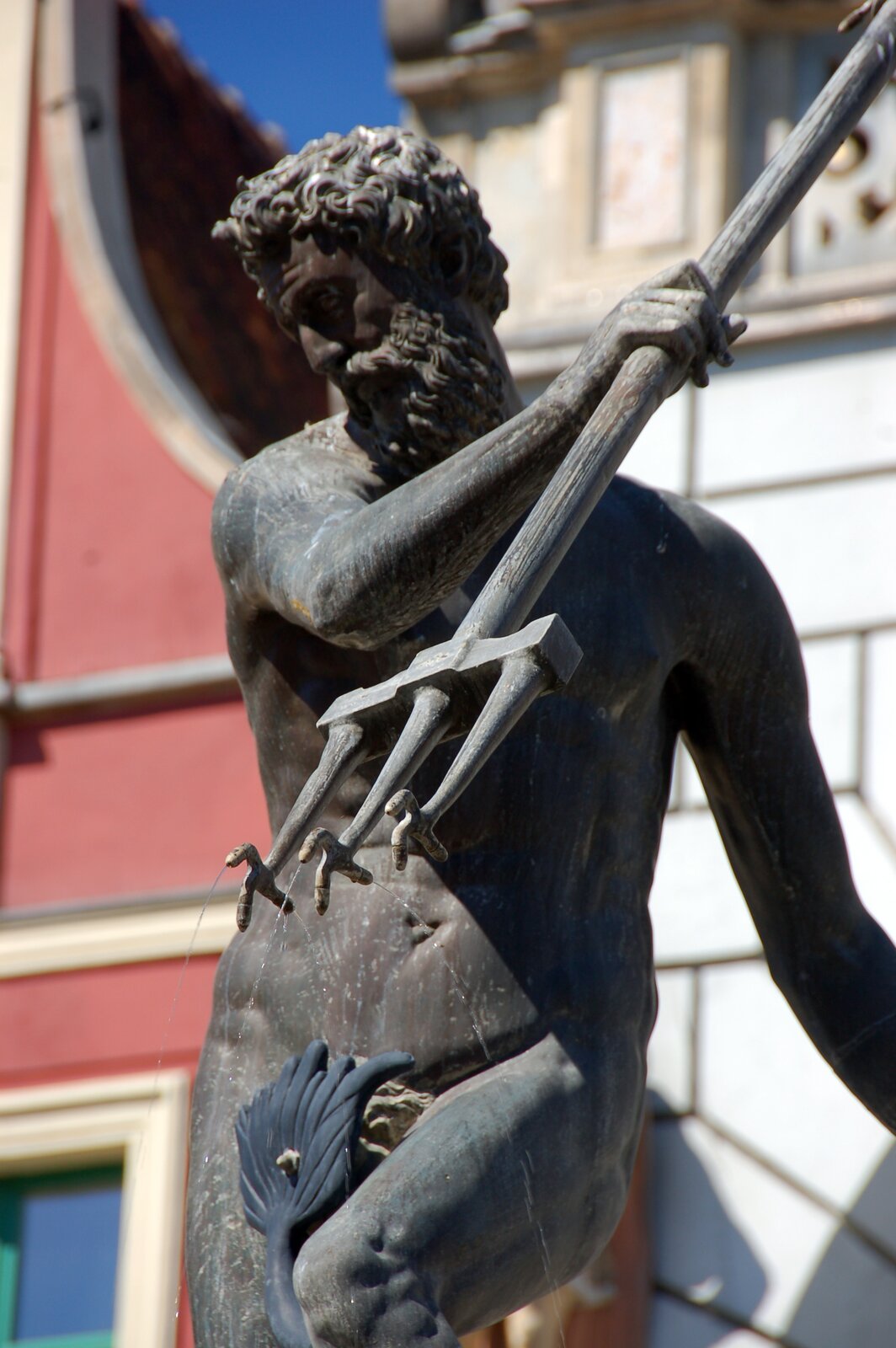 Ilustracja przedstawia posąg Neptuna zdobiący fontannę w Gdańsku. Rzeźba wykonana jest z ciemnego kamienia. Bóg ukazany jest w ruchu. Lewą rękę ma skierowaną do tyłu; w prawej unosi do góry trójząb. Głowę ma przechyloną w bok. Lewe kolano ma lekko uniesione dla zachowania równowagi