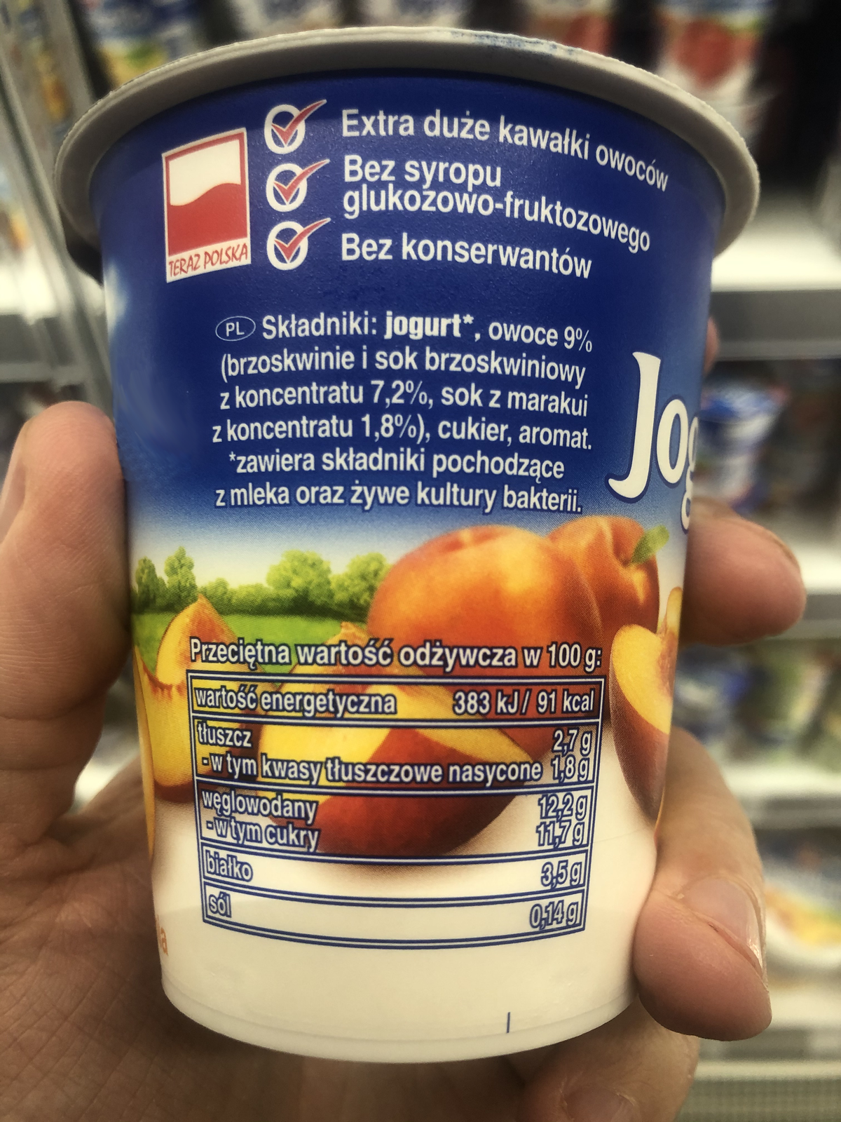 Ilustracja przedstawia etykietę jogurtu. Zawarto na niej następujące informacje: Extra duże kawałki owoców, Bez syropu glukozowo-fruktozowego, Bez konserwantów. Składniki: jogurt*, owoce 9% (brzoskwinie i sok brzoskwiniowy z koncentratu 7,2%, sok z marakui z koncentratu 1,8%), cukier, aromat. * zawiera składniki pochodzące z mleka oraz żywe kultury bakterii. Przeciętna wartość odżywcza w 100g: wartość energetyczna 383kJ/91 kcal; tłuszcz 2,7g (w tym kwasy tłuszczowe nasycone 1,8g); węlowodany 12,2g (w tym cukry 11,7g); białko 3,5g; sól 0,14g.