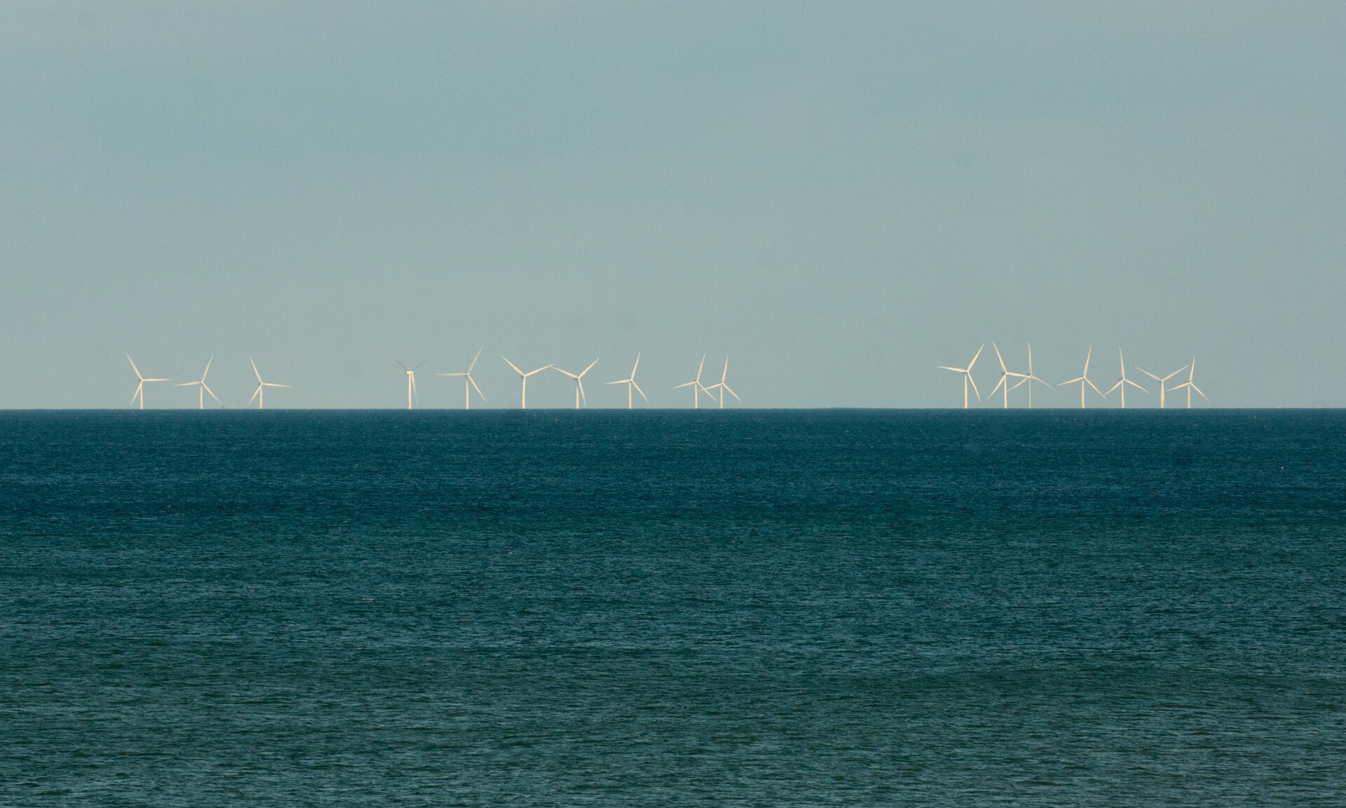 Zdjęcie przedstawia zbiornik wodny. W tle na brzegu widać liczne wiatraki elektrowni wiatrowej.  