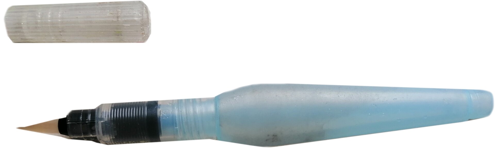 Zdjęcie przedstawia pędzelek wodny. Widoczny jest pędzel wodny w poziomie, od prawej strony widoczny jest korpus ze zbiorniczkiem i rękojeścią w kolorze jasnoniebieskim, zakończony trójkątnym elementem osadzonym w korpusie. U góry po lewej widoczny jest cylindryczny biały półprzeźroczysty element.