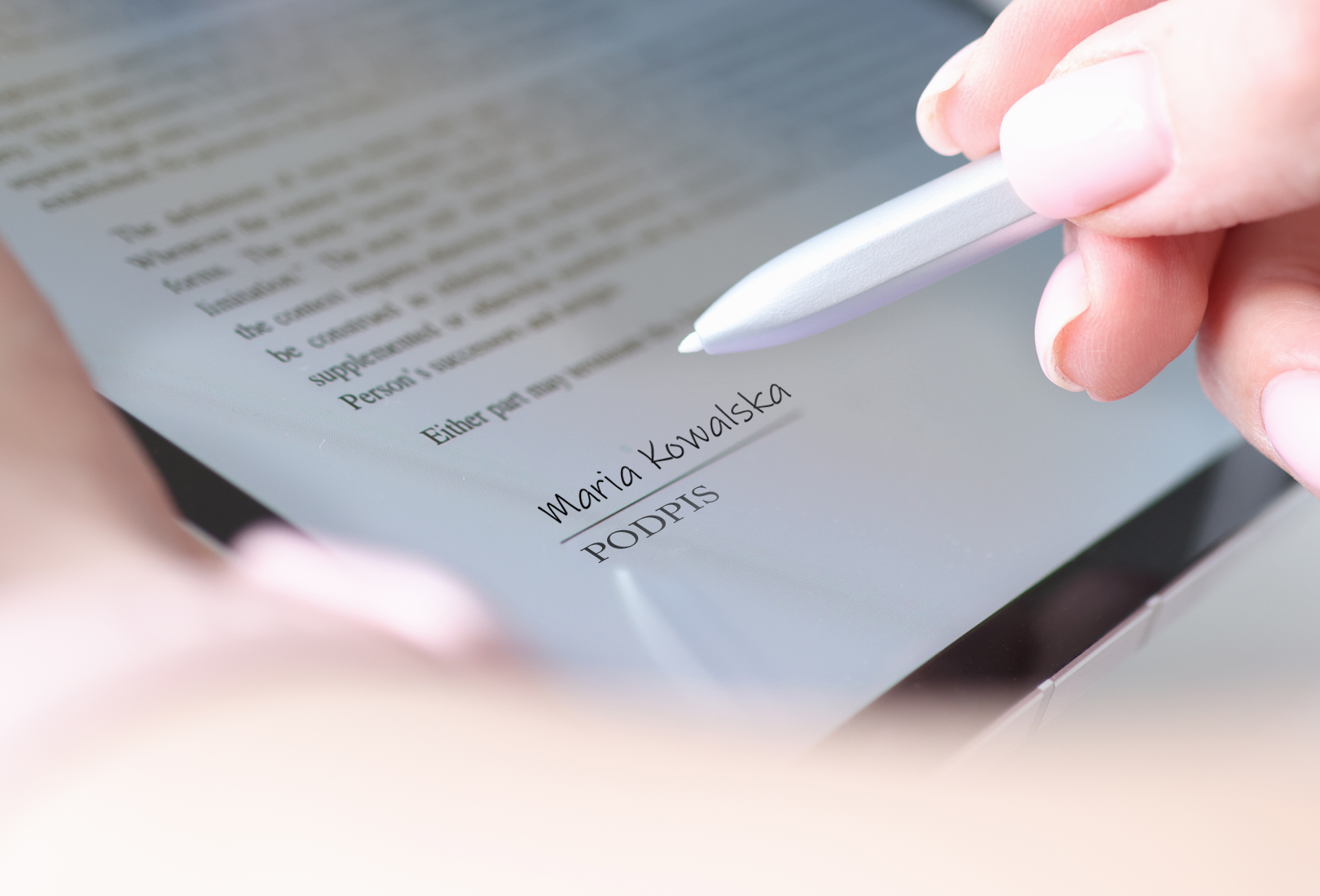Kliknij aby powiększyć Na zdjęciu tablet z tekstem. W jego lewym rogu widać drukowanymi literami słowo podpis a nad nim odręcznym pismem napisane: Maria Kowalska. W prawym górnym rogu widać dłoń trzymającą długopis. Z lewej strony fragment dłoni podtrzymującej tablet.