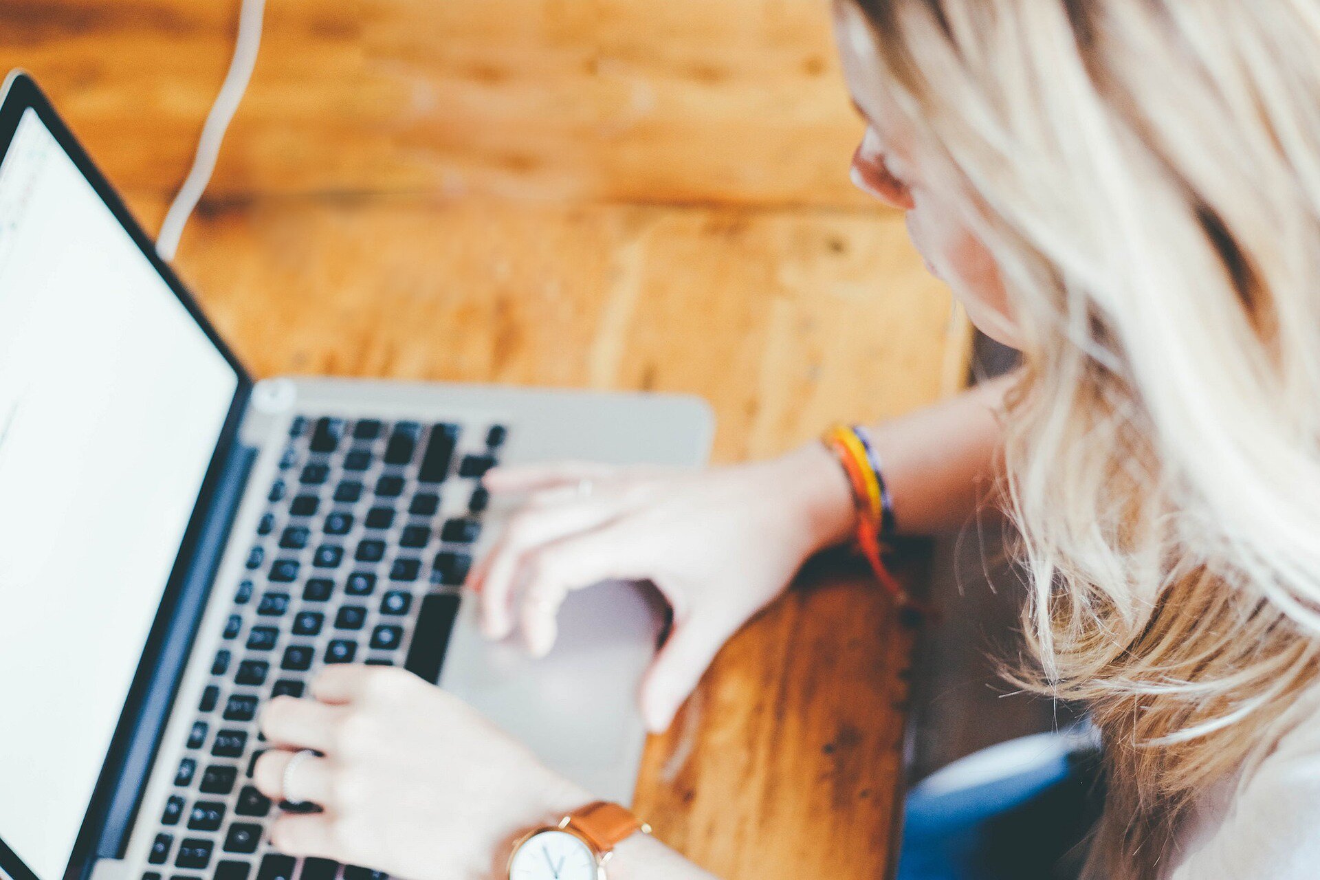 Na zdjęciu widoczna jest młoda kobieta, siedząca przy biurku, skupiona nad klawiaturą laptopa, który leży na blacie.