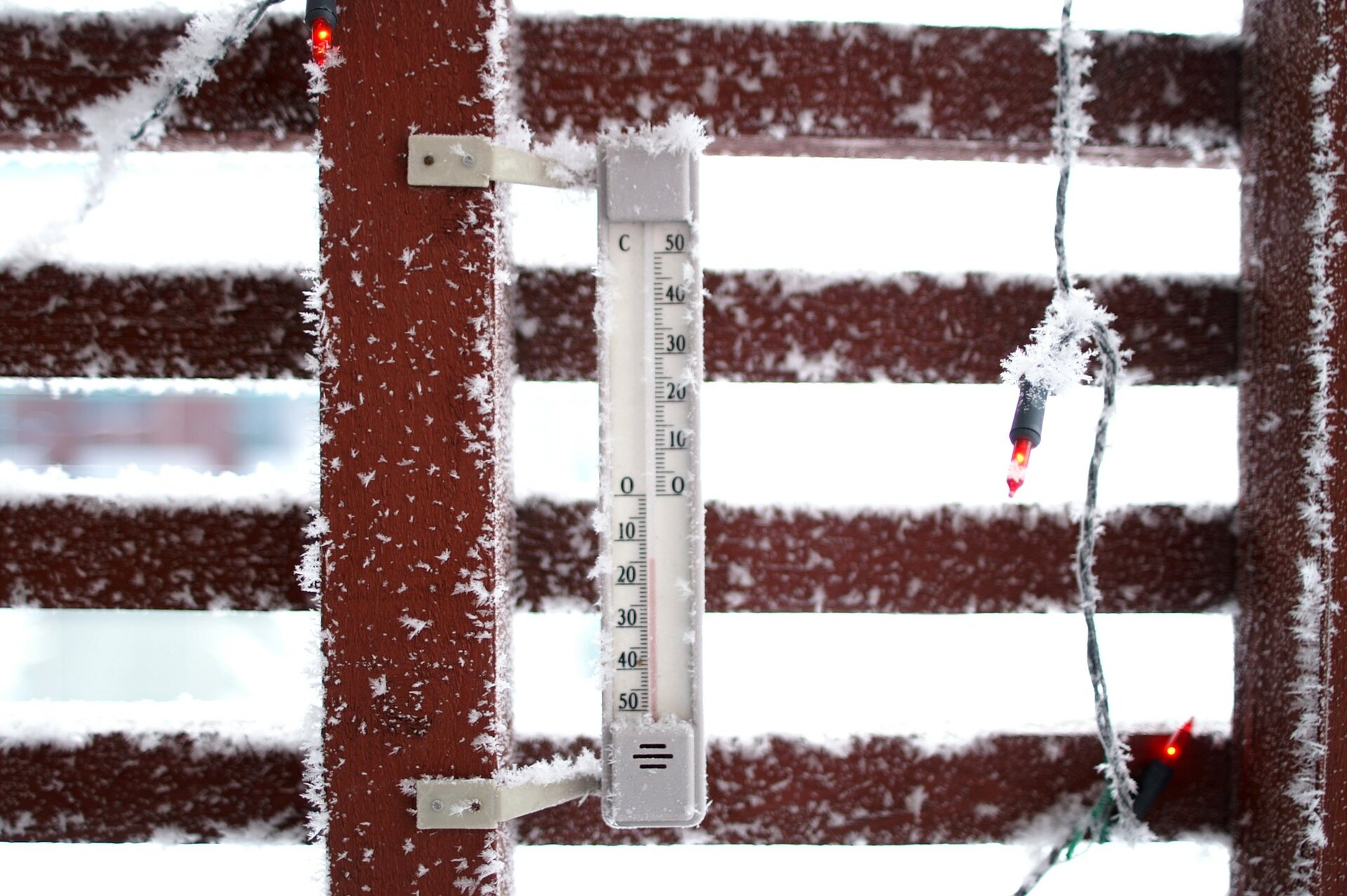 Zdjęcie przedstawia termometr meteorologiczny zaokienny. Zamontowany jest na ścianie budynku za oknem. Ma on podłużny kształt. Przez jego środek biegnie rurka na ciecz. Na środku termometru widać kreskę z wartością zero. Poniżej wartości są ujemne, powyżej dodatnie.