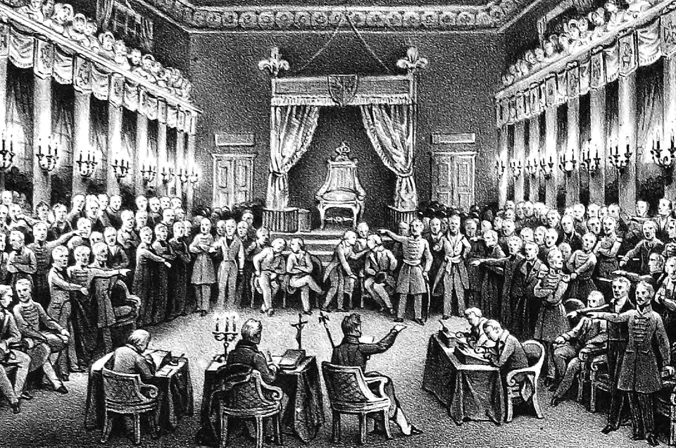Ilustracja przedstawia wysoką salę. Po bokach sali stoją grupy mężczyzn w surdutach. Wskazują na siebie palcami. Na środku na krzesłach oraz przy stolikach siedzą mężczyźni. Część notuje coś na kartkach. Pozostali intensywnie dyskutują. W tle stoi tron, który otaczają zasłony. Po bokach sali stoją kolumny oraz są świeczniki na ścianach.