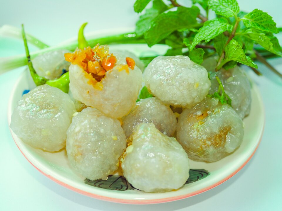 Zdjęcie przedstawia okrągłe kluski na talerzu. Przypominają pyzy. Jedna z klusek jest rozcięta - widać w środku nadzienie koloru pomarańczowego. Talerz przyozdobiony jest gałązkami mięty.