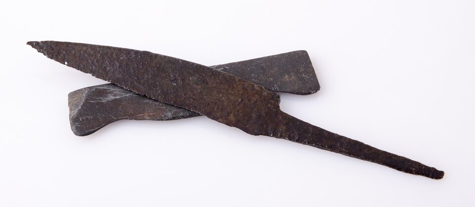 Ilustracja przedstawia nóż żelazny wraz z narzędziem do jego ostrzenia, czyli osełką. Nóż ma szerokie ostrze, następnie węższy trzonek do trzymania. Osełka ma kształt niewielkiego prostokąta.   