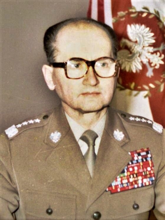 Zdjęcie przedstawia dojrzałego mężczyznę w mundurze generalskim. Mężczyzna siedzi, za nim znajduje się polski sztandar z godłem.