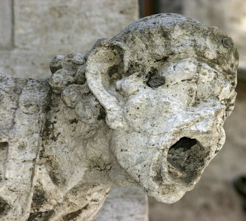 Zdjęcie przedstawia głowę posągu wykonanego z jasnego materiału. Głowa jest zniszczona, ma braki, w niektórych miejscach jest ciemna.  