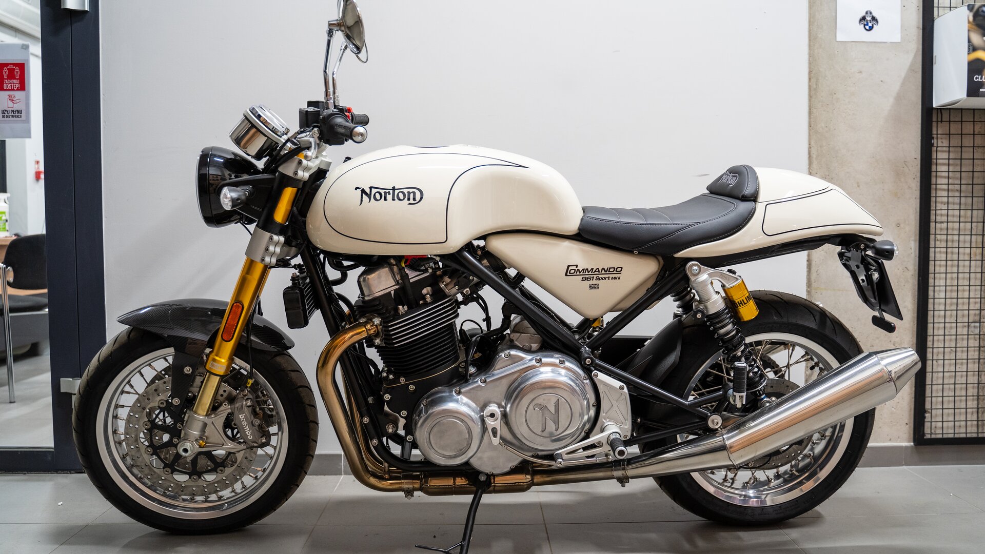 Zdjęcie przedstawia model motocykla Norton Commando 961 Sport MK2. Motocykl ma chromowane elementy, obudowa baku, karoseria za siedzeniem oraz pod siedzeniem są koloru jasnobeżowego. Na baku jest napis Norton.  