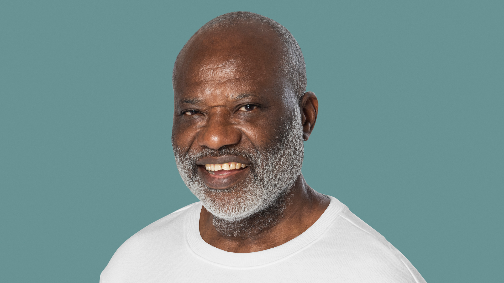 Zdjęcie przedstawia starszego, ciemnoskórego, łysego mężczyznę z siwą brodą. Mężczyzna jest postawny i ma brązowe oczy.