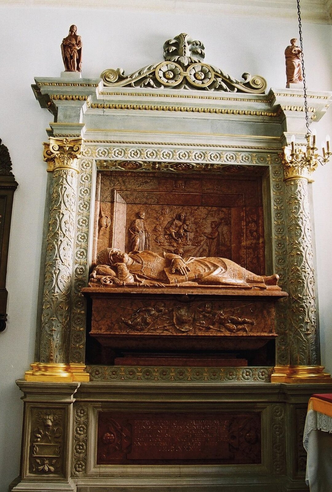 Ilustracja o kształcie pionowego prostokąta przedstawia fotografię  nagrobka biskupa Piotra Tomickiego, autorstwa Bartolomea Berrecciego. Ukazuje leżącego biskupa w pozycji bocznej na tumbie. Za nim znajduje się ściana z przedstawianiem figuralnym. Nagrobek wykonany jest z brązowego marmuru, a dekoracja dokoła z białego. Po bokach znajdują się kolumny ze złotymi kapitelami. Całość wieńczy szeroki gzyms z figurkami. 