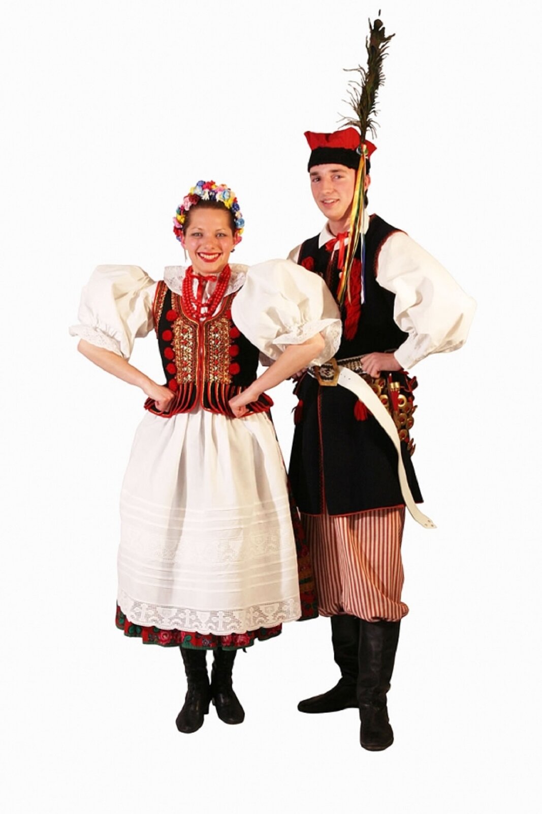 Ilustracja przedstawia parę w stroju do krakowiaka. Kobieta ma na sobie spódnicę do połowy łydki,zapaskę, bogato zdobiony cekinami i haftem serdaczek. Mężczyzna ubrany jest w białą koszulę, czarną sukmanę, pasiaste spodnie oraz czerwoną rogatywkę, z czarnym, barankowym otokiem i pękiem pawich piór. Do pasa krakowiaka przyczepione są brzęczące kółeczka.