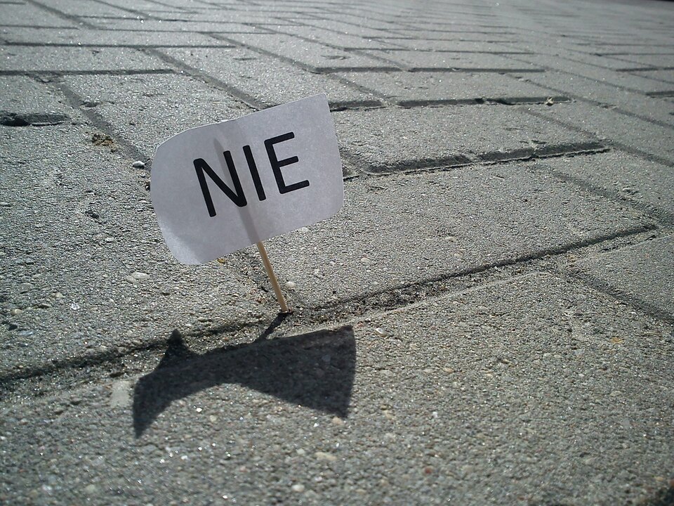Zdjęcie przedstawia chodnik wyłożony kostką brukową. Pomiędzy kostkami wbita jest na patyczku kartka z napisem NIE.