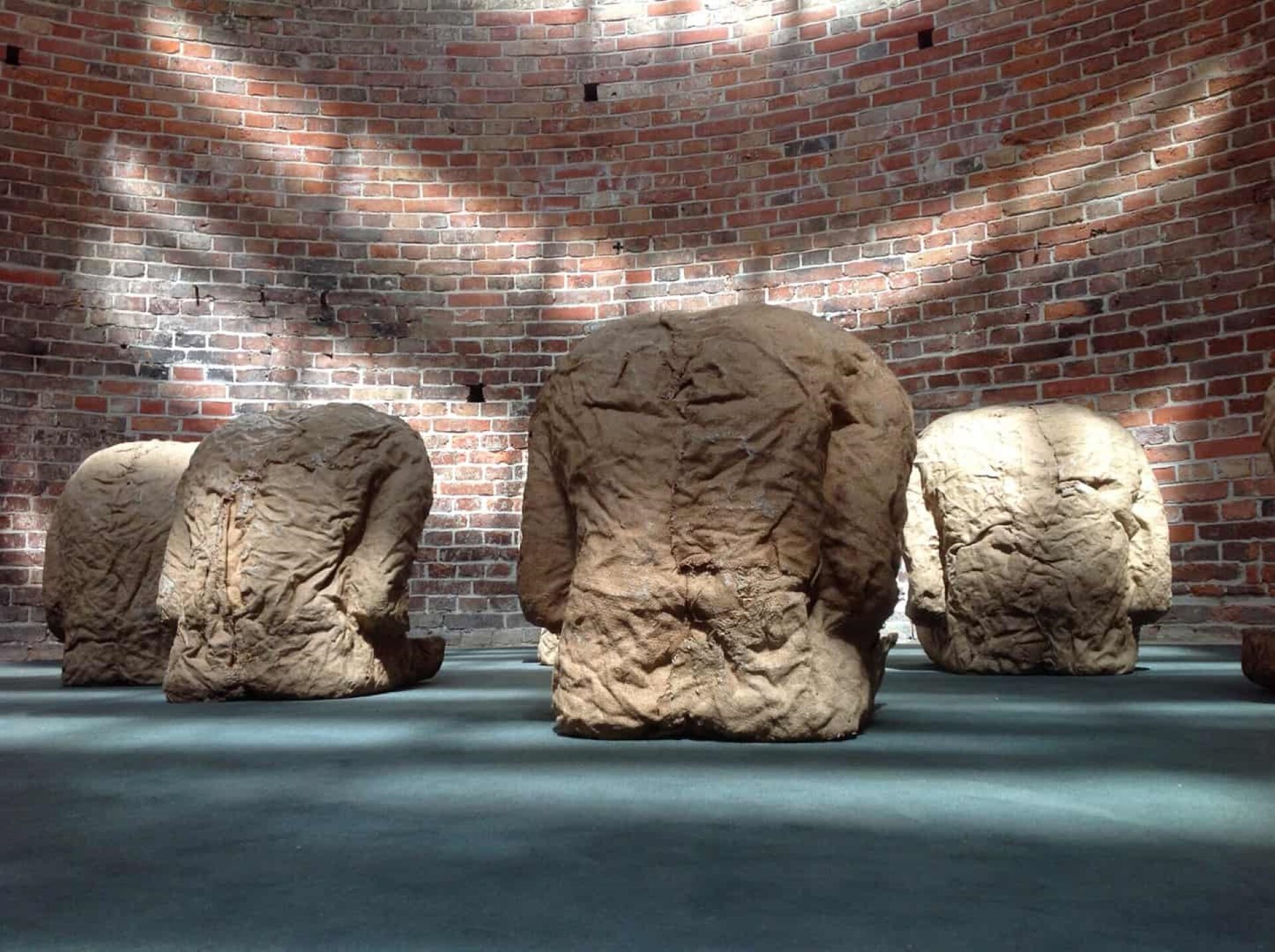 Praca Magdaleny Abakanowicz pod tytułem „Plecy” przedstawia grupę figur, które kształtem przypominają siedzących ludzi pozbawionych kończyn i głów. Faktura figur wyglądem przypomina pogniecioną tkaninę. Figury zwrócone są plecami do widza. Instalacja stoi na jasnej podłodze w pomieszczeniu o okrągłych ścianach z cegły.