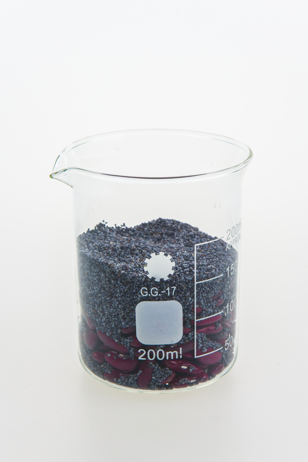 Zdjęcie przedstawia mak leżący na fasoli w jednej zlewce. Mak zaczyna się przesypywać przez fasolę i osiadać na dnie zlewki.