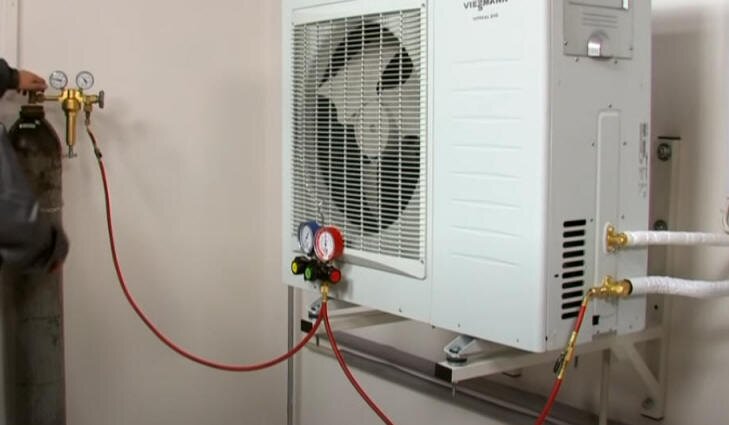 Na zdjęciu przedstawiono przebieg testu szczelności układu czynnika chłodniczego pompy ciepła. Do jednostki zewnętrznej podłączono przewodami butlę z azotem. Na przewodach znajdują się manometry wskazujące wartość ciśnienia.