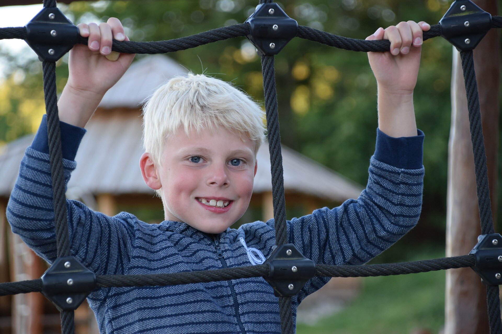 Zdjęcie przedstawia chłopca, który wspina się na ściankę zbudowaną ze sznurów.