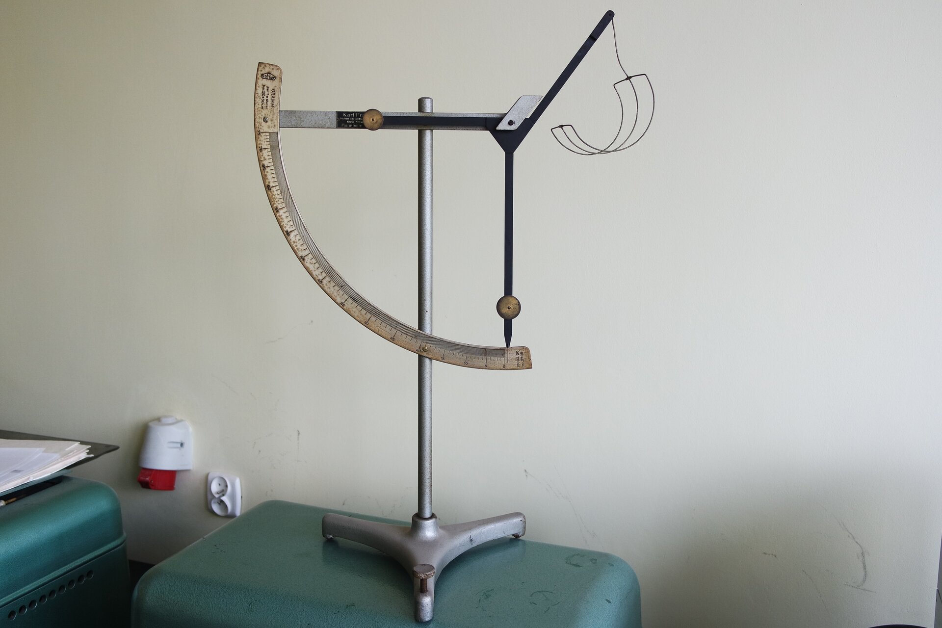 Zdjęcie przedstawia wagę kwadrantową do oznaczania gramatury. Urządzenie zbudowane jest ze stojaka, do którego przymocowana jest skala pomiarowa, i dwuramiennej dźwigni.