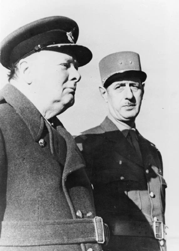 Kliknij, aby powiększyć Dwóch mężczyzn na fotografii stoi obok siebie. Mężczyzna po lewej ubrany jest w wojskowy płaszcz i patrzy przed siebie, mężczyzna po prawej, ubrany w wojskowy mundur, patrzy na tego po lewej.