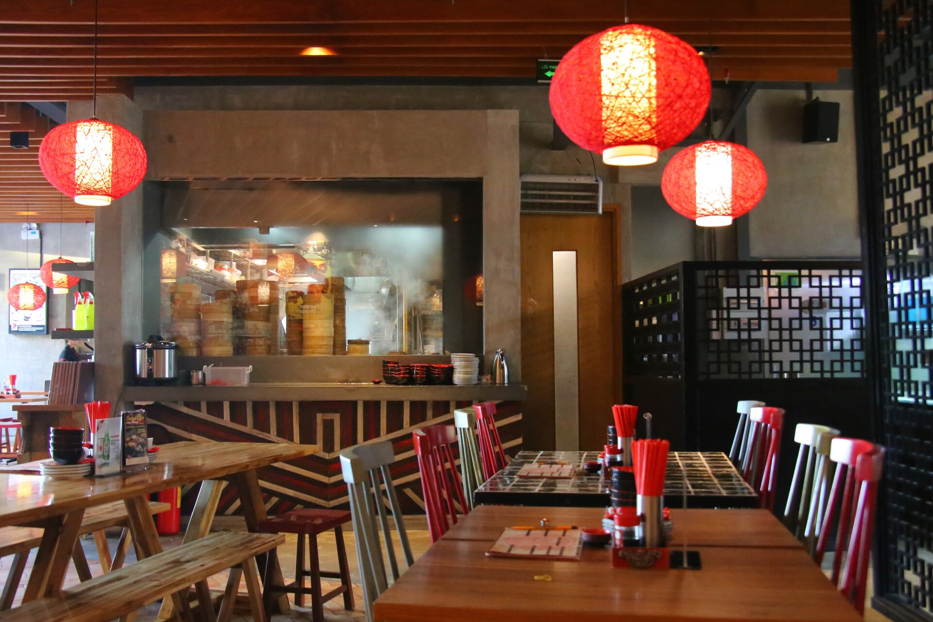 Zdjęcie przedstawia wnętrze restauracji chińskiej. Na stołach stoją naczynia z pałeczkami, a pod sufitem zawieszone są lampy przypominające okrągłe lampiony.