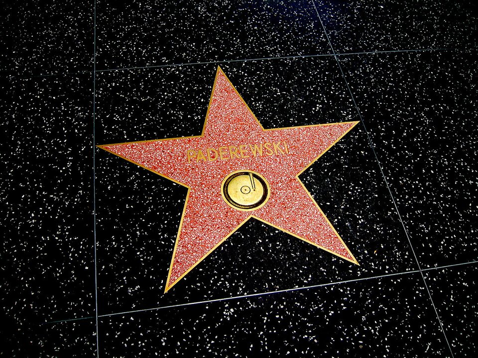Zdjęcie przedstawia fragment posadzki. Na czarnym kamieniu wyróżnia się czerwony ułożony w kształcie gwiazdy. Wokół niej oraz w jej centralnym miejscu żółta lamówka. Powyżej napis: Paderewski. To Aleja gwiazd w Hollywood. 