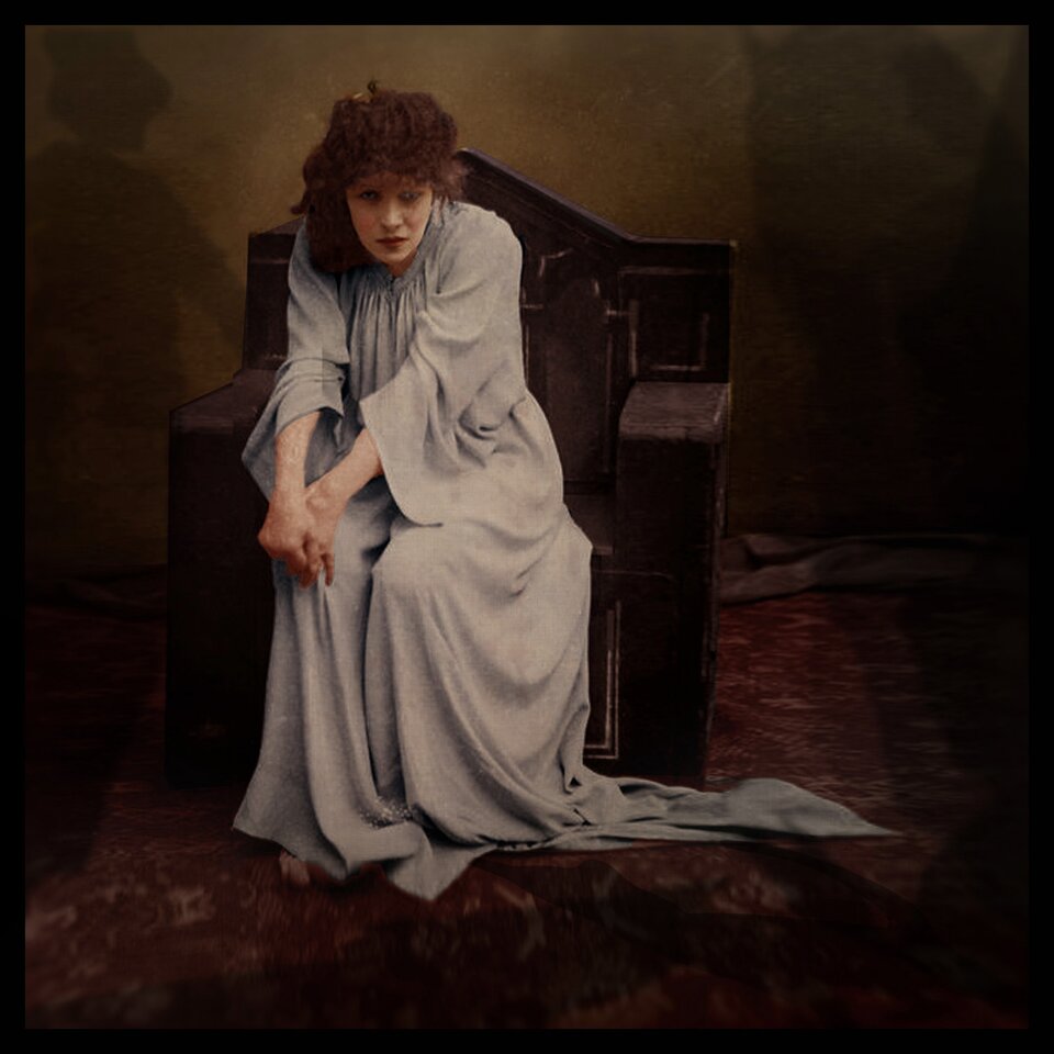 Zdjęcie przedstawia młodą kobietę. Ubrana jest w długą suknię siedzi na fotelu, jest lekko pochylona. Ma wyciągnięte przed siebie dłonie, które zdaje się myć bez wody.