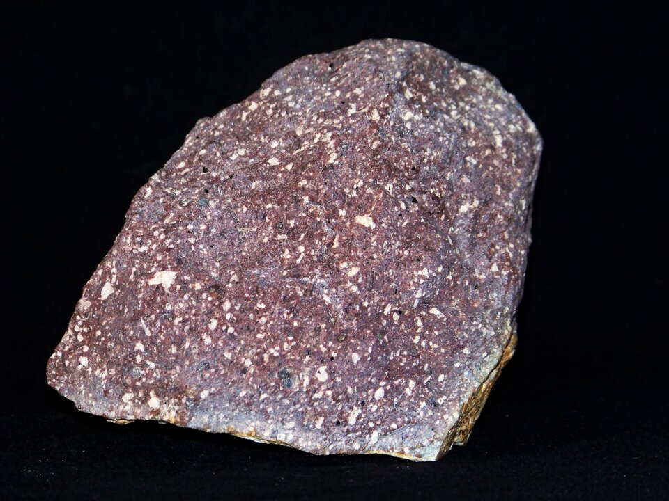 Zdjęcie przedstawia porfir. Posiada chropowatą powierzchnię o czerwonawej barwie z domieszkami białego.