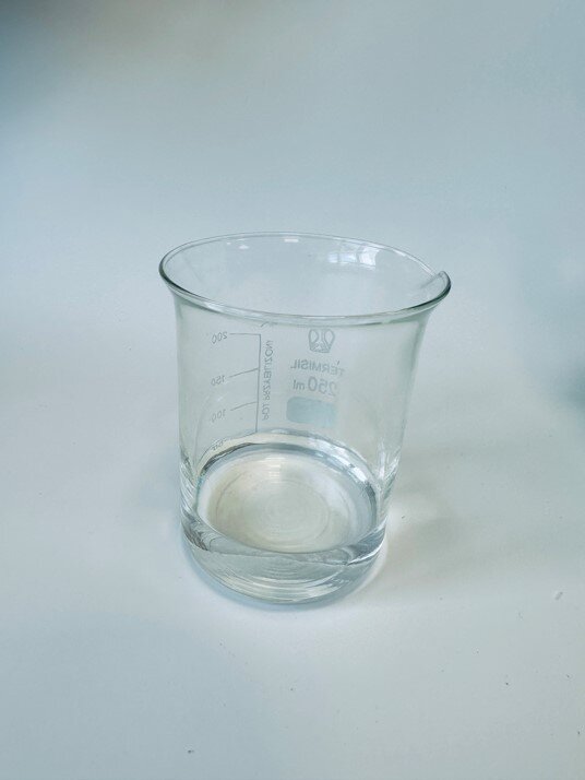 Zdjęcie przedstawia szklane naczynie z przezroczystą cieczą - etanolem.
