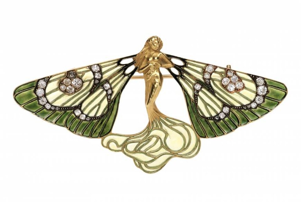 Ilustracja przedstawia pracę René Jule Lalique pochodzącą z ok. 1900 roku. Na fotografii widzimy broszę w kształcie motyla. Na środku znajduje się złota figurka postaci ze skrzydłami. Przyozdobione są one kryształkami.