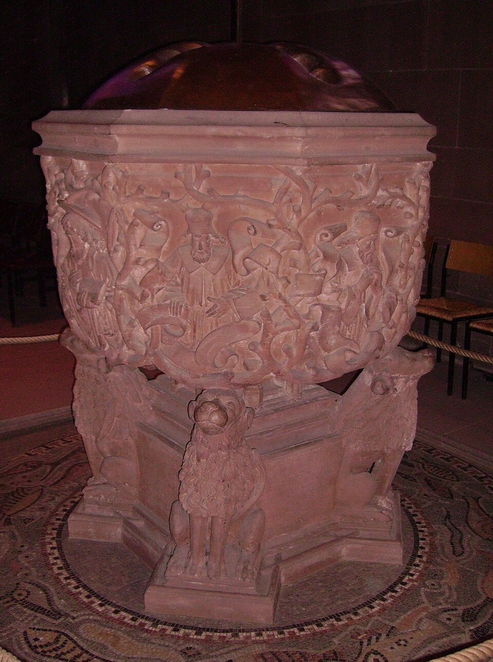 Na zdjęciu znajduje się chrzcielnica z katedry w Wormacji w Niemczech. Jest wykonana z brązowego kamienia, misę chrzcielną wspierają pełnoplastyczne postaci siedzących zwierząt przypominających psy. Bogata dekoracja znajduje się na zewnętrznych ściankach misy. Wśród licznych nagich sękatych gałęzi znajdują się płaskorzeźbione popiersia proroków starotestamentowych.