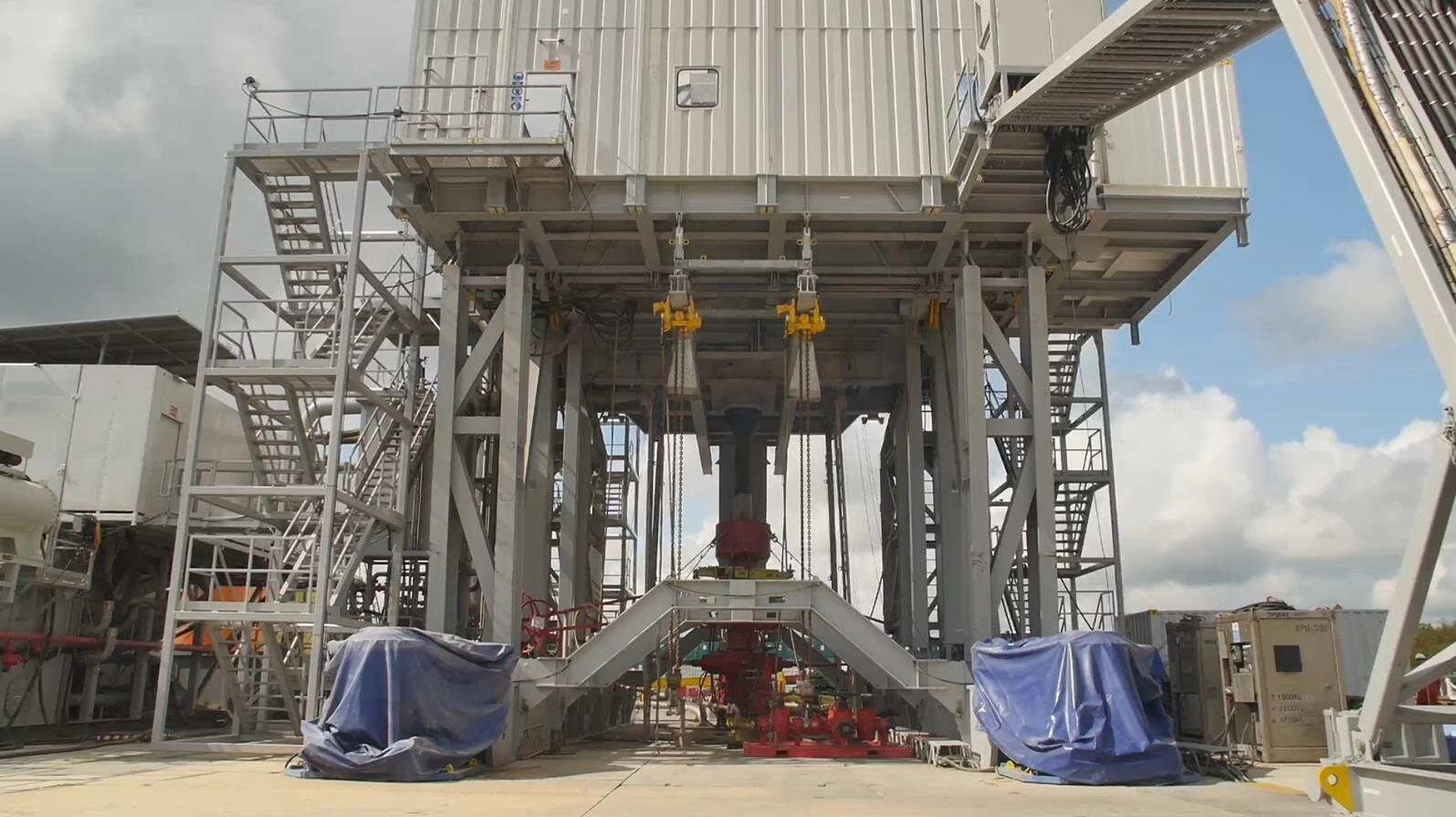 Na zdjęciu widoczna jest podbudowa wieżomasztu. Podbudowa wieżomasztu składa się z grubych stalowych podpór zapewniających nośność osadzonego na nim galerii. Na galerii widocznej w górnej części zdjęcia znajduje się budynek wykonany z blachy falistej. Po obu naprzeciwległych bokach wieżomasztu znajdują się schody prowadzące na galerię. Schody przypominają układ z rusztowaniem. Po środku galerii widać biegnący w dół cylindryczny element o dużej średnicy zakończony głowicą eksploatacyjną. Głowica jest w kształcie litery H. Przed głowicą widoczny jest układ rur. 