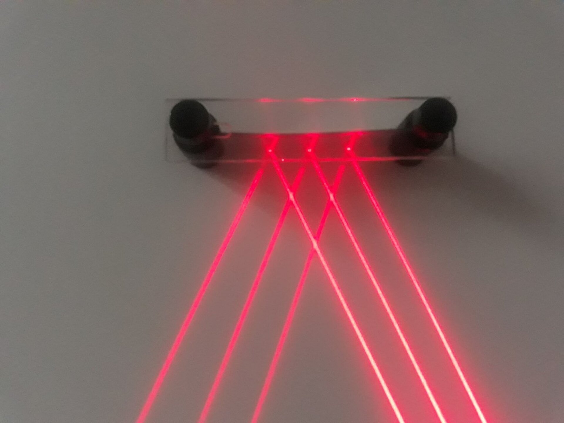 Ilustracja przedstawia, jak działa prawo odbicia światła w praktyce. Z prawego dolnego rogu wydostają się trzy czerwone równoległe promienie laserowe, które padają na powierzchnię płaską pod pewnym kątem, tę powierzchnię stanowi kawałek blaszki. Równoległe wiązki światła zachowują równoległość również po odbiciu od blaszki. Odbijają się pod takim samym kątem, jak kąt padania i biegną po odbiciu dokładnie tak samo równolegle jak przed nim.