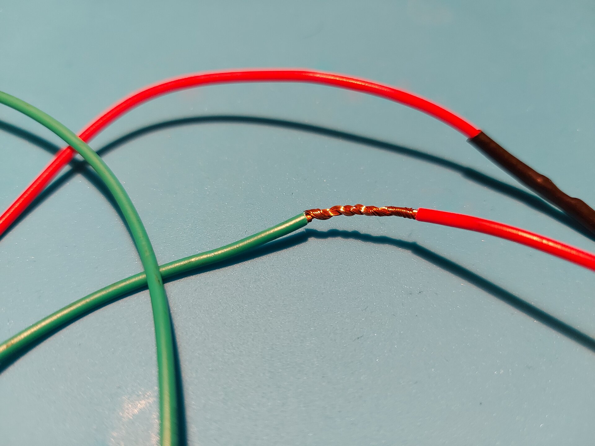 Zdjęcie przedstawia 2 przewody z usuniętą izolacją tym samym odsłaniając miedziane wnętrze, które skręcono ze sobą ustawiając miedziane zakończenia końcami przeciwnymi u podstawy następnego kabla.